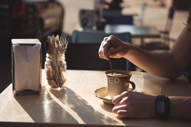 Человек, помешивающий кофе ложкой за столом — стоковое фото