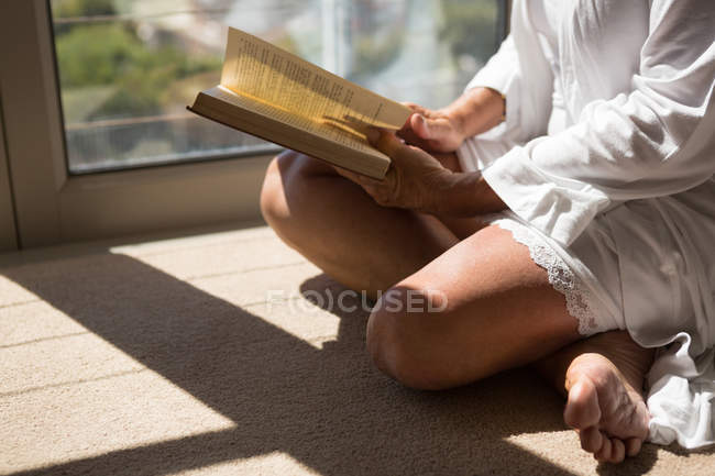 Donna disabile leggere libro vicino alla finestra a casa . — Foto stock