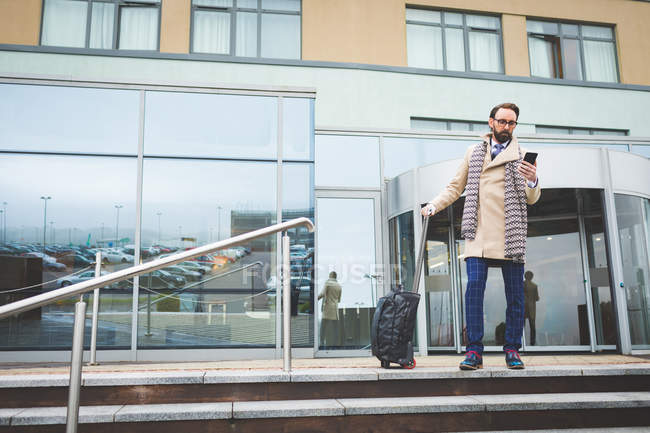 Uomo d'affari che esce dall'hotel mentre usa il cellulare in una giornata di sole — Foto stock