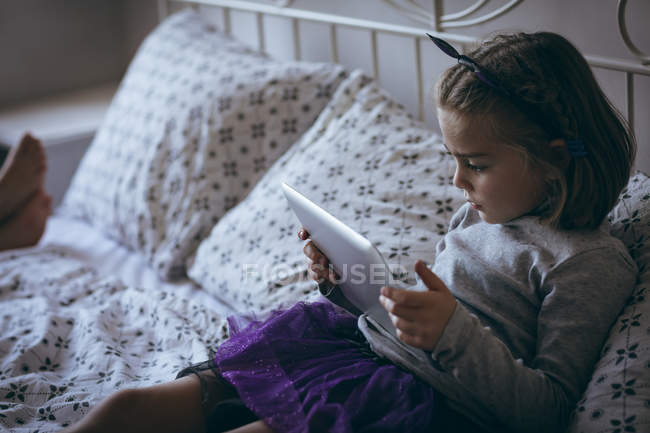 Девочка с цифровым планшетом на кровати в спальне — стоковое фото