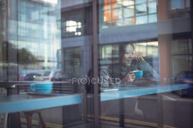 Красива жінка розмовляє по мобільному телефону, маючи каву в кафетерії — стокове фото