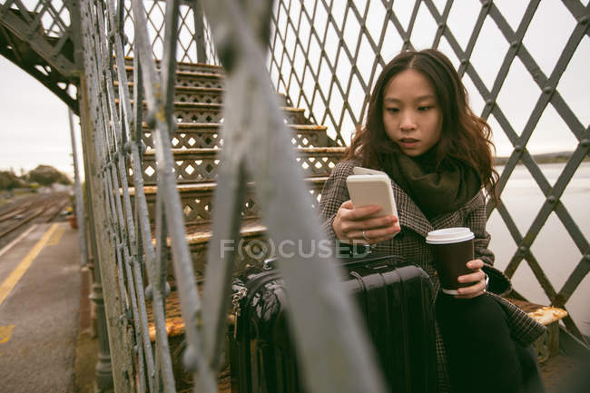 Женщина, использующая мобильный телефон на лестнице на железнодорожной платформе — стоковое фото