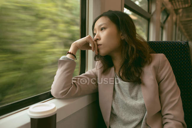 Femme réfléchie regardant par la fenêtre tout en voyageant dans le train — Photo de stock