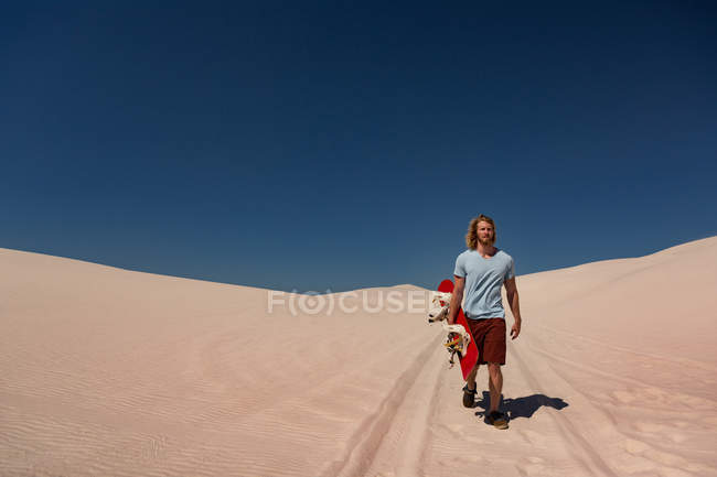 Человек с песчаной доской ходит по пустыне в солнечный день — стоковое фото