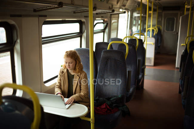 Червоне волосся молода жінка використовує свій ноутбук у потязі — стокове фото