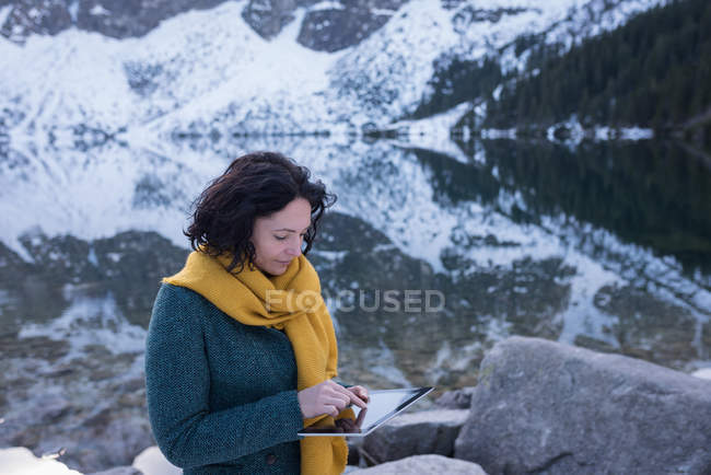 Female hiker using digital tablet at lakeside during winter — Stock Photo