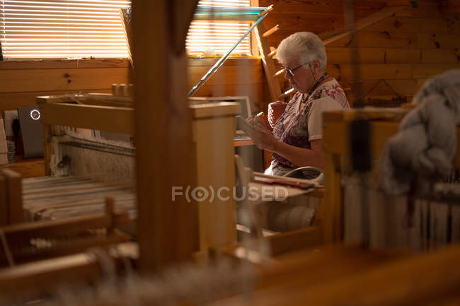 Active senior woman weaving silk at shop — Stock Photo