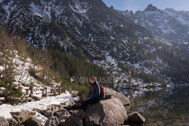 Female hiker sitting on rock at lakeside during winter — Stock Photo