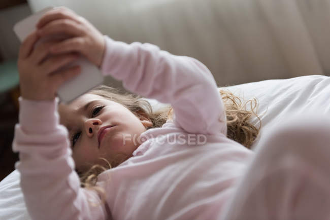 Kleines Mädchen benutzt Handy im Schlafzimmer zu Hause — Stockfoto