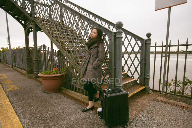 Задуманная женщина, опирающаяся на перила на железнодорожной платформе — стоковое фото