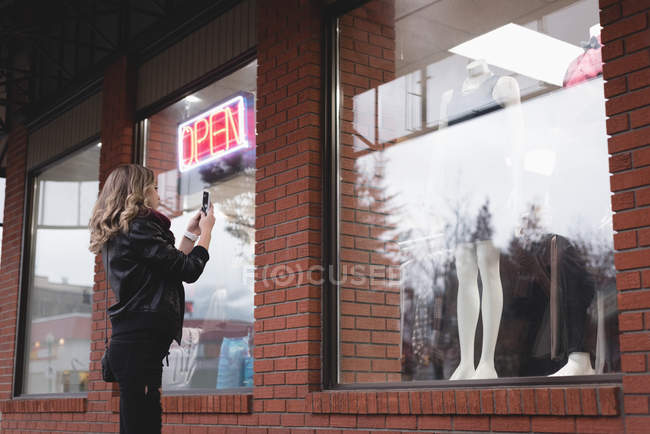 Girl taking picture of dress with mobile phone in passage — Stock Photo