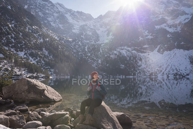 Wanderin sitzt im Winter auf Felsen am Seeufer — Stockfoto