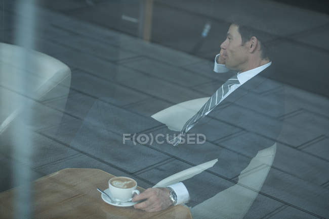Бізнесмен розмовляє на мобільному телефоні, маючи каву в офісі — стокове фото