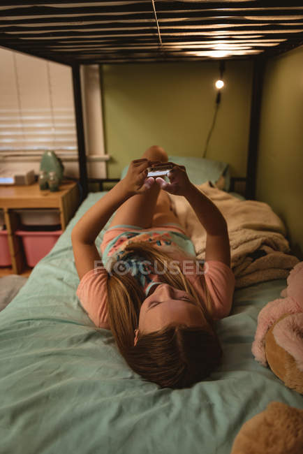 Menina deitada na cama e usando telefone celular em casa . — Fotografia de Stock