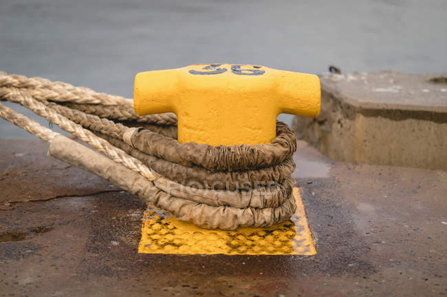 Old mooring bollard with rope tied on pier in shipyard — Stock Photo