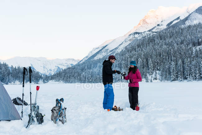 Coppia in piedi insieme e la condivisione di bevande calde nel paesaggio innevato durante l'inverno . — Foto stock