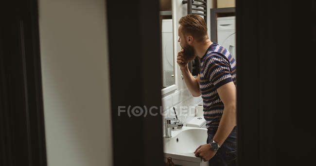 Человек смотрит на себя в зеркало в ванной комнате — стоковое фото