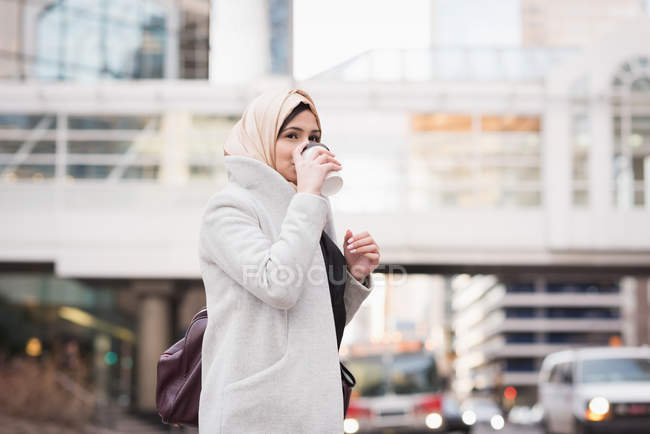 Femme en hijab buvant du café dans la rue de la ville — Photo de stock