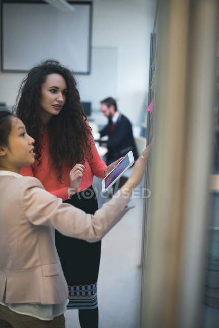 Female executives discussing over sticky notes in office — Stock Photo