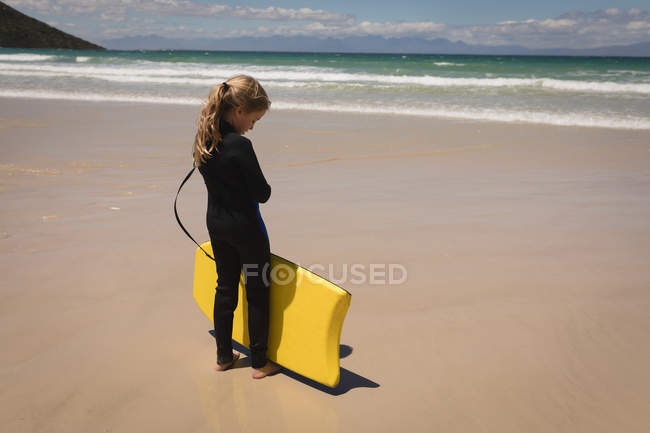 Nachdenkliches Mädchen steht mit Surfbrett am Strand — Stockfoto