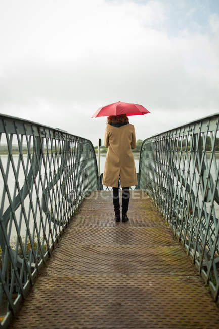 Vista trasera de la mujer de pie con paraguas en la estación de tren - foto de stock