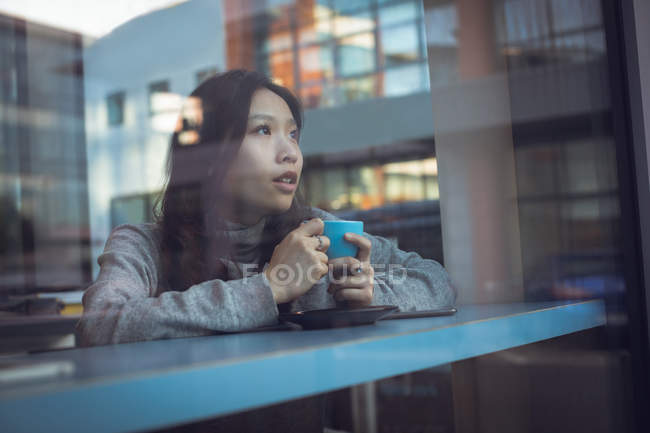 Thoughtful woman having coffee at table in cafeteria — Stock Photo
