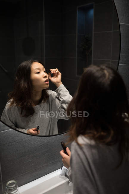 Mulher aplicando rímel na frente do espelho — Fotografia de Stock