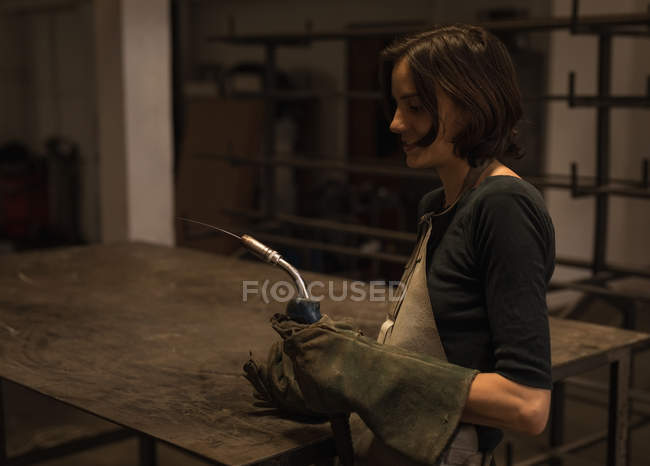 Female welder holding welding torch in workshop. — Stock Photo