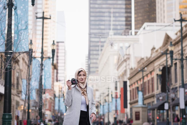 Femme en hijab en cliquant sur les photos avec appareil photo numérique sur la rue de la ville — Photo de stock