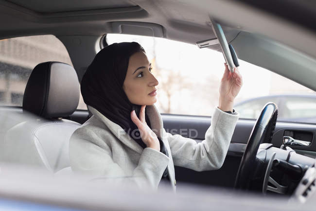 Mujer joven en hijab mirando al espejo retrovisor - foto de stock