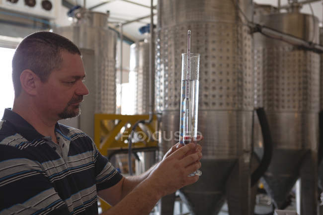 Trabalhador masculino examinando gin em cilindro de medição na fábrica — Fotografia de Stock