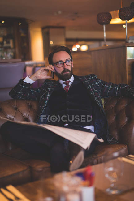 Businessman taking on mobile phone while reading newspaper in hotel — Stock Photo