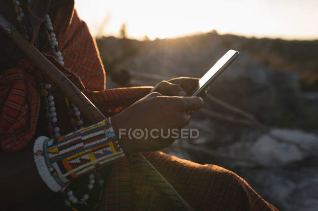 Maasai man in traditional clothing using mobile phone at countryside — Stock Photo