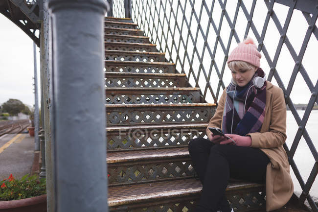 Hermosa mujer sentada en las escaleras y usando el teléfono móvil - foto de stock