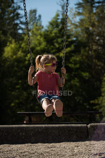Jolie fille jouer sur swing dans parc — Photo de stock