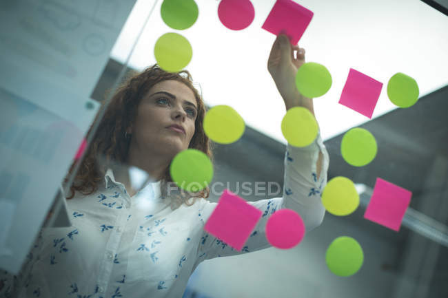 Femmina esecutivo attaccare note adesive sulla parete di vetro in ufficio — Foto stock