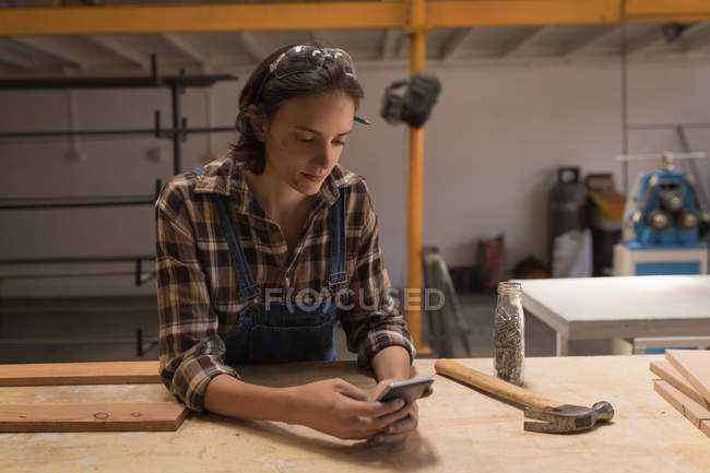 Junge Kunsthandwerkerin benutzt Handy in Werkstatt. — Stockfoto