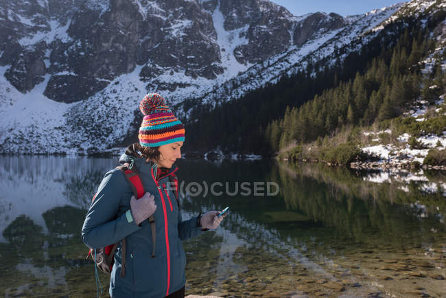 Randonneuse utilisant un téléphone portable au bord du lac pendant l'hiver — Photo de stock