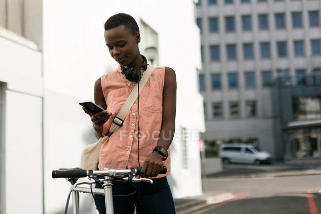 Mujer con bicicleta usando teléfono móvil en la calle de la ciudad - foto de stock