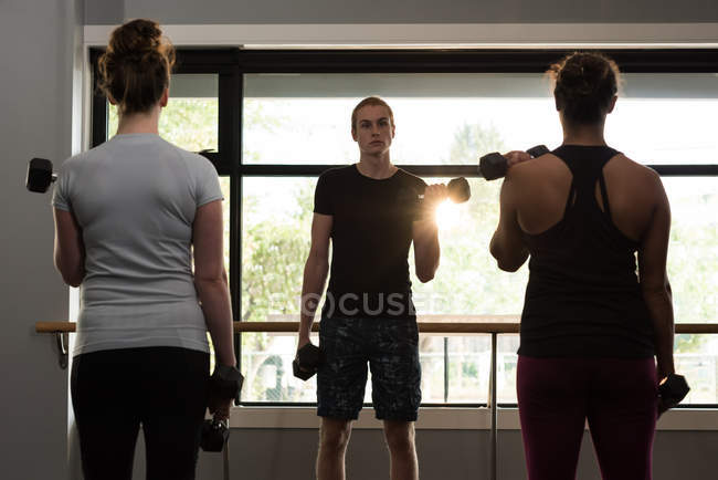 Trainer assisting women in exercising with dumbbells at fitness studio. — Stock Photo
