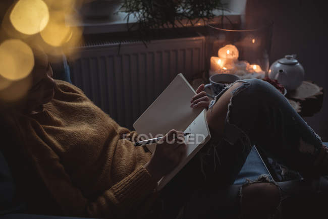 Woman writing in the diary against lit candle — Stock Photo