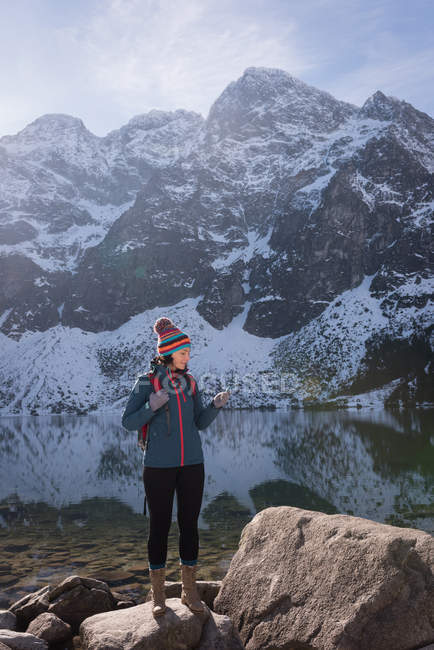 Wanderin nutzt Handy im Winter am Seeufer — Stockfoto