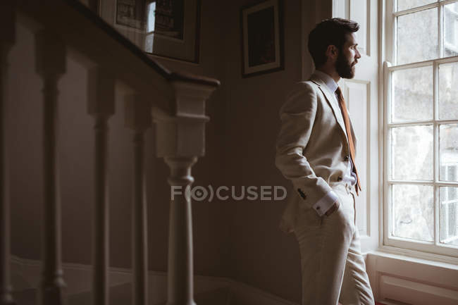 Thoughtful groom standing at the window and looking out — Stock Photo
