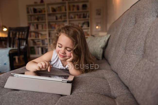 Усміхнена дівчина лежить на дивані і використовує цифровий планшет у вітальні вдома — стокове фото