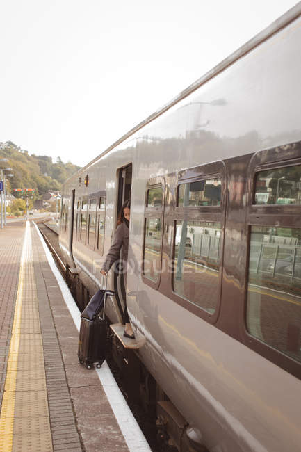 Femme monter dans le train avec des bagages au quai ferroviaire — Photo de stock