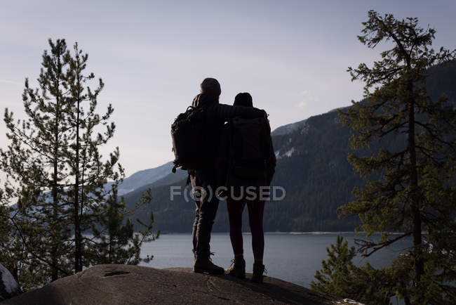 Вид сзади на пару туристов, стоящую на скале возле реки в солнечный день — стоковое фото