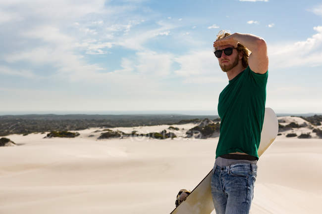 Homem com sandboard de pé no deserto em um dia ensolarado — Fotografia de Stock