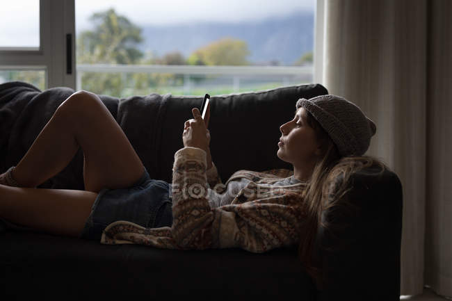 Frau benutzt Handy im heimischen Wohnzimmer, Seitenansicht. — Stockfoto