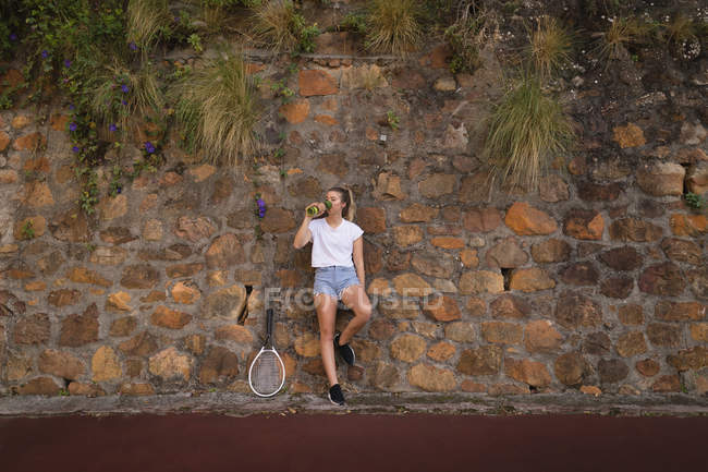 Femme fatiguée boire de l'eau dans le court de tennis — Photo de stock