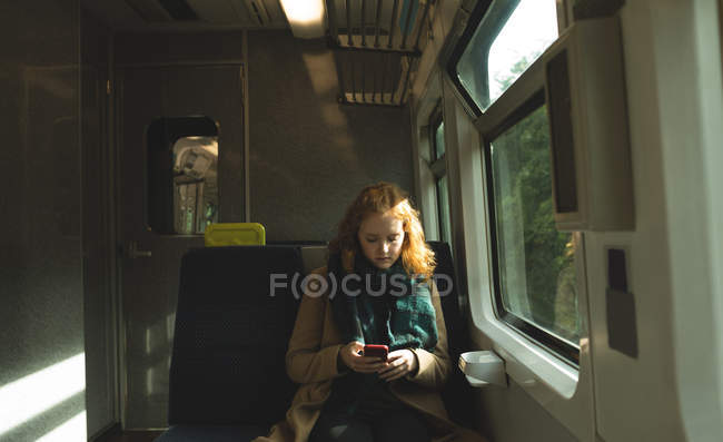 Giovane donna che utilizza il telefono cellulare mentre viaggia in treno — Foto stock